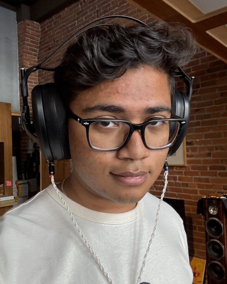 Jake, the engineer building Vellic, in profile wearing open-back headphones in front of a brick wall and a pair of studio speakers.